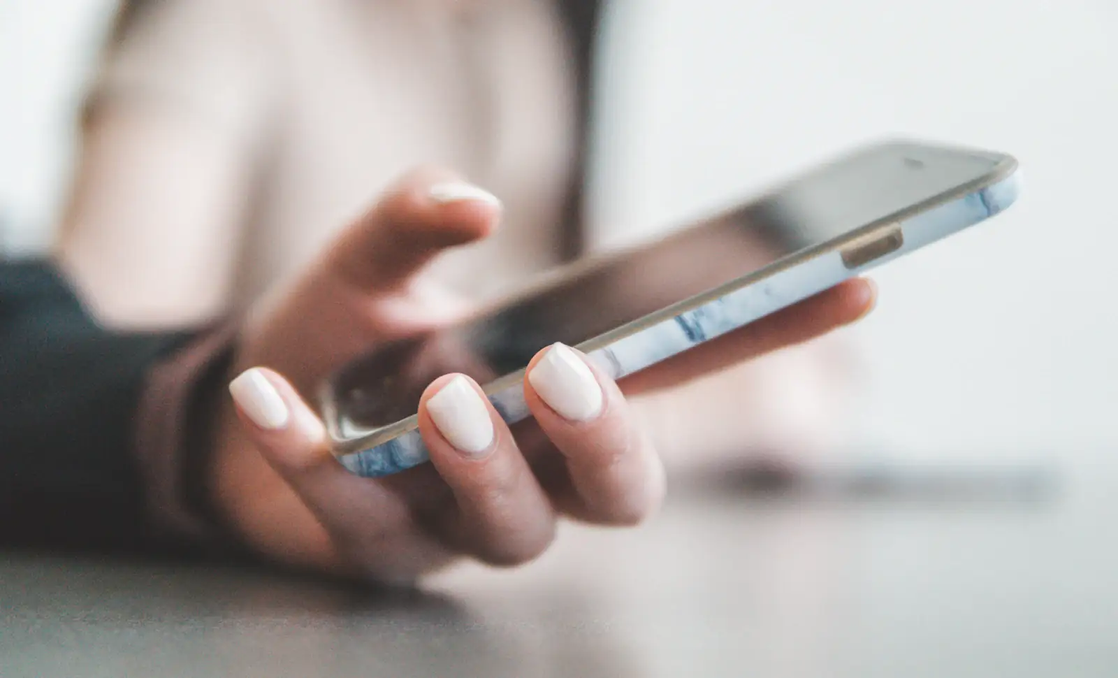 Manicured hands holding a phone in a bright, softly lit room