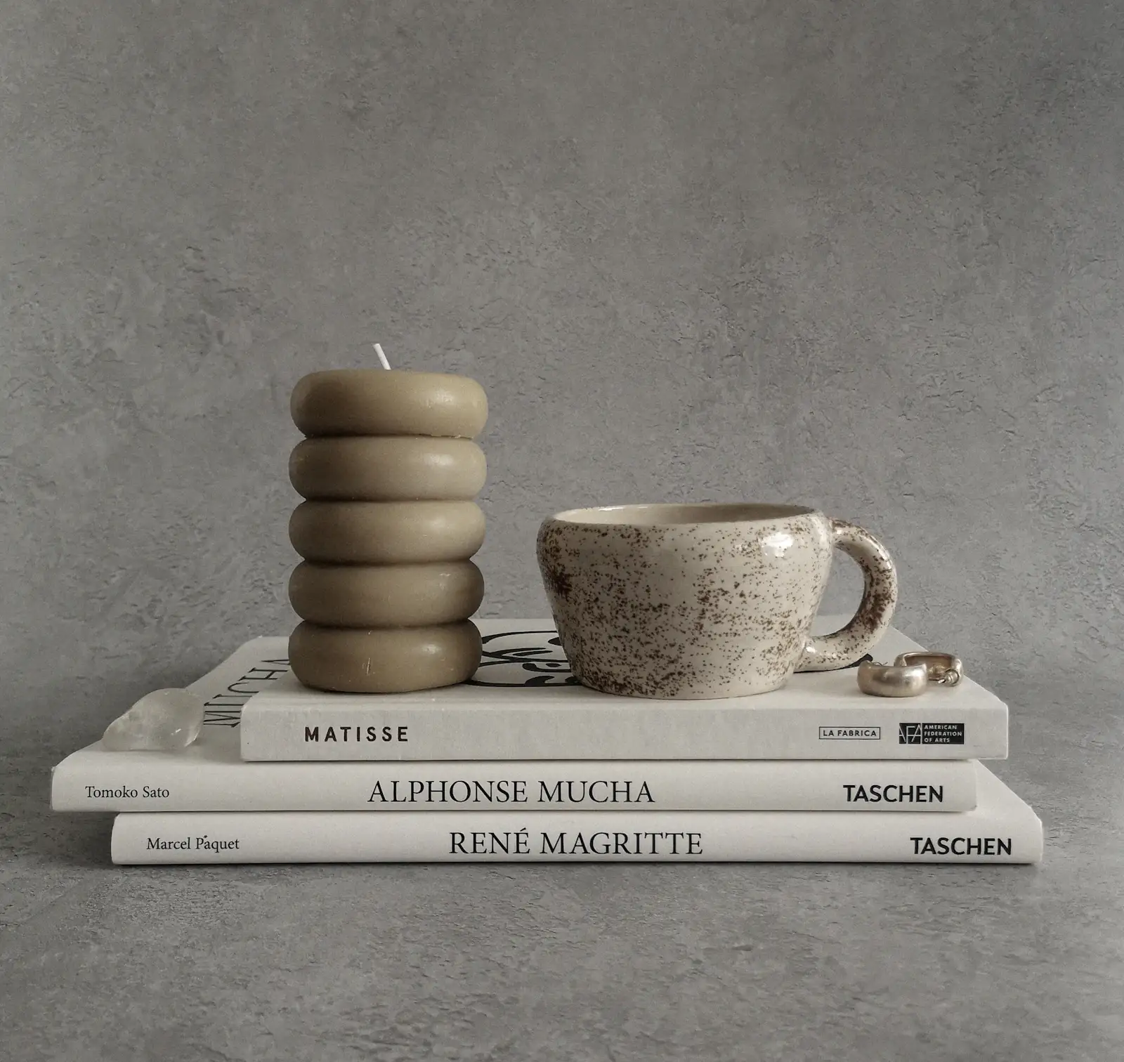 Stacked art books with a sculptural candle and stoneware cup against a stone wall